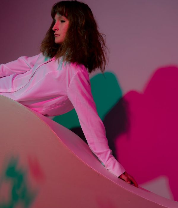 Woman in a calm yoga pose in a dark studio with pink light.